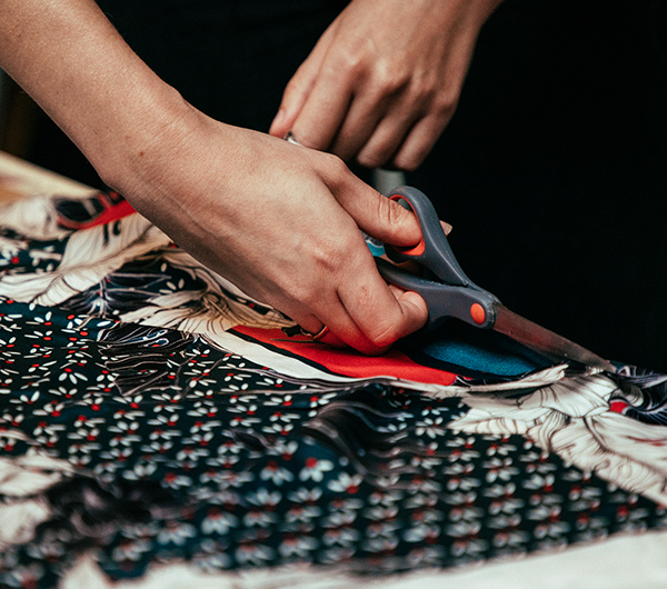 A woman hand is shown cutting into a printed black, white and red fabric using scissors