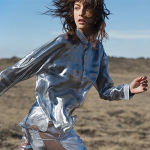 A model is wearing a metalic silver shirt and trousers with a desert in background